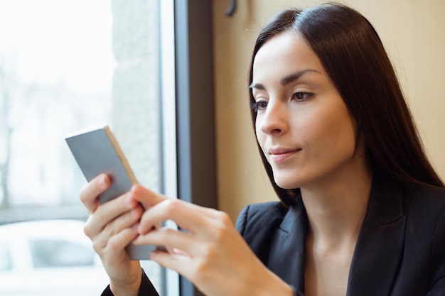 Portrait de jeune belle femme travaillant au téléphone ou utilisant Internet assis dans un café