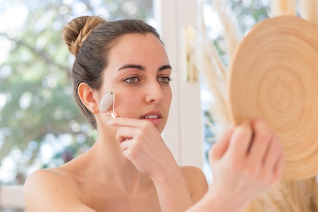 Portrait de jeune belle femme utilisant un rouleau de quartz rose sur son visage