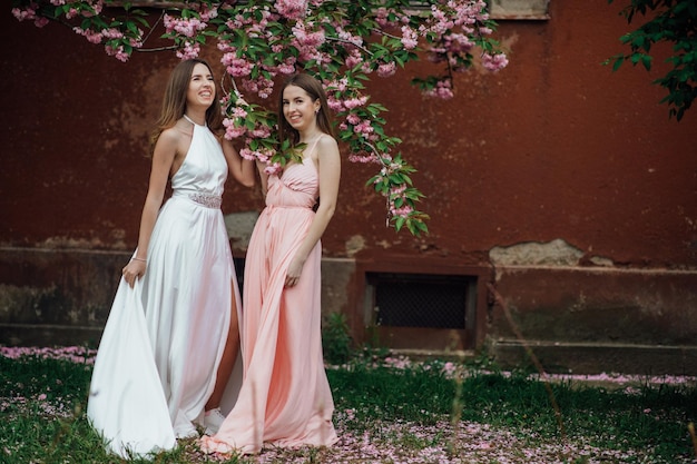 Portrait de jeune belle fille à la mode posant près d'un arbre fleuri avec des fleurs roses.