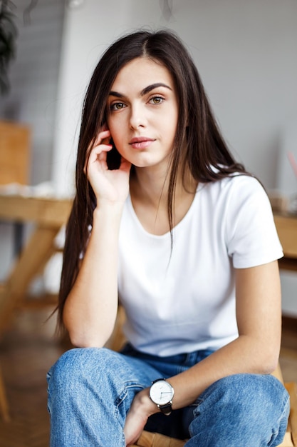 Portrait de jeune belle fille porte un t-shirt blanc assis sur une chaise en bois à l'intérieur