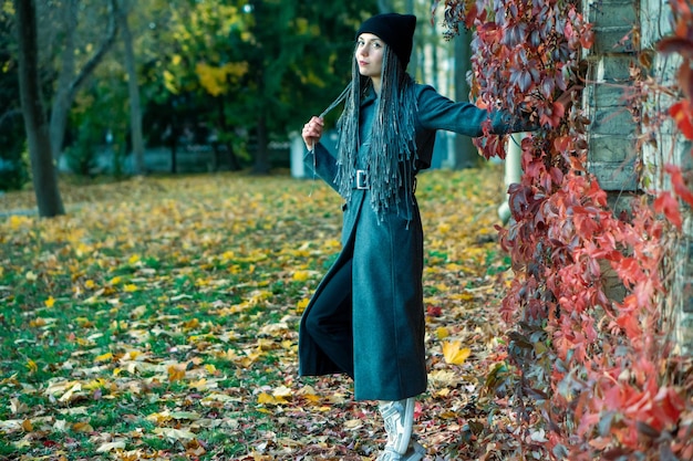Photo portrait d'une jeune belle fille avec un sourire sur le visage dans un parc d'automne sur un fond de feuilles colorées une fille avec des dreadlocks et des queues de cochon pose sur le fond des arbres