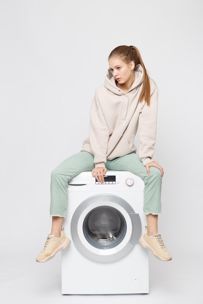 Portrait de jeune belle jeune fille assise sur une machine à laver et regardant la caméra isolée sur fond blanc