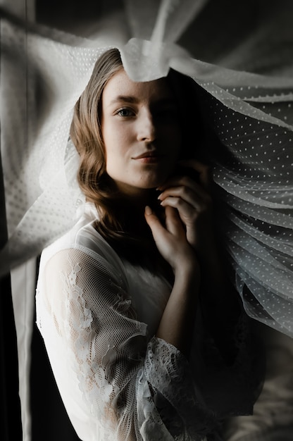 Portrait d'une jeune et belle mariée pendant les préparatifs du matin le jour du mariage. belle fille tient un voile sur sa tête. matin de mariage de la mariée.