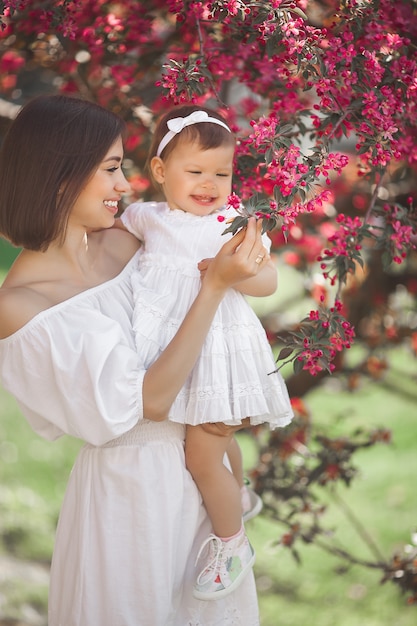 Portrait de jeune belle mère avec sa petite fille. Gros plan d'une famille aimante. Jolie femme tenant son enfant en fleurs roses et souriant.