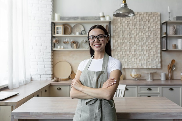 Portrait d'une jeune blogueuse femme debout à la maison dans la cuisine dans un tablier et regardant le