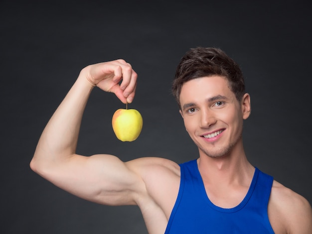 Portrait de jeune bodybuilder souriant tenant une pomme sur fond noir.