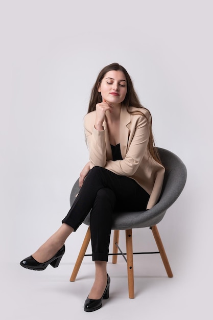 Portrait d'une jeune brune aux cheveux longs dans le studio Jolie fille assise sur une chaise sur un fond blanc