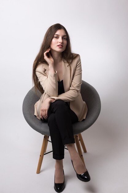 Portrait d'une jeune brune aux cheveux longs dans le studio Jolie fille assise sur une chaise sur un fond blanc