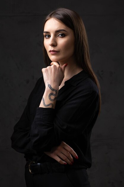 Portrait d'une jeune brune aux cheveux longs en studio Photo dramatique dans des couleurs sombres Une fille avec un tatouage de serpent sur son bras