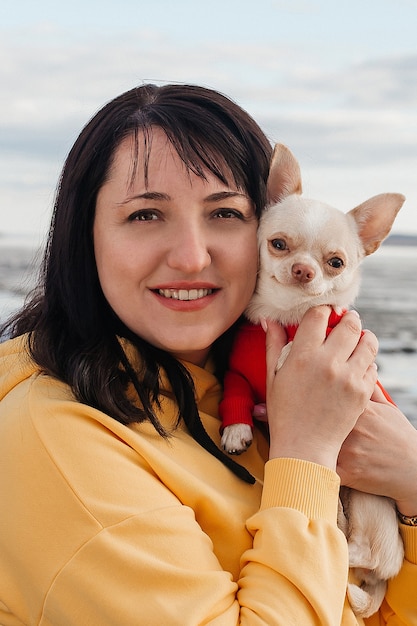 Photo portrait d'une jeune brune dans la nature avec un chien chihuahua dans ses bras. la fille sourit à la caméra.