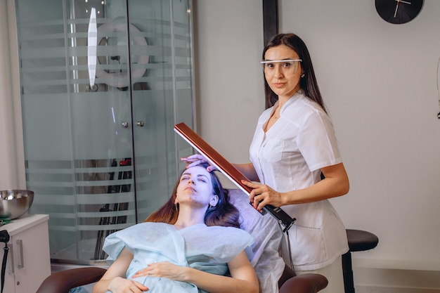 Le portrait d'une jeune cliente sympa et d'un dermatologue du lieu de la procédure de cosmétologie.