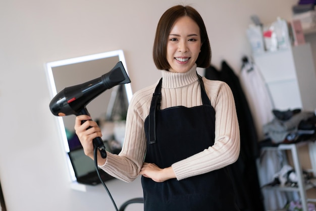 Portrait d'une jeune coiffeuse asiatique tenant des outils de coupe de cheveux qualifiés