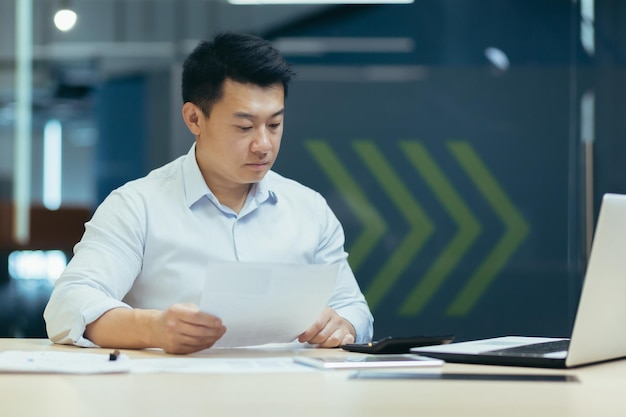 Portrait de jeune comptable asiatique sérieux et concentré travaillant avec des documents et une calculatrice