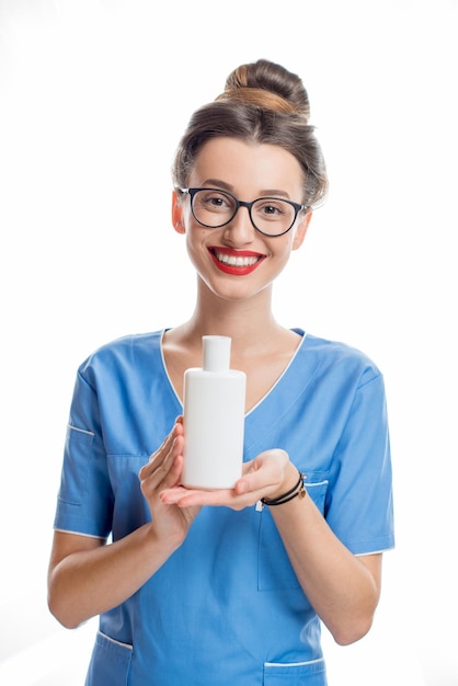 Portrait d'un jeune cosmétologue souriant tenant une bouteille de cosmétiques. Tourné en studio isolé sur fond blanc