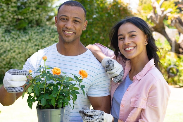 Portrait d'un jeune couple afro-américain souriant avec un pot de fleurs tout en se tenant au jardin