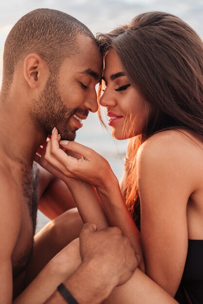 Portrait de jeune couple aimant tendre assis sur la plage ensemble