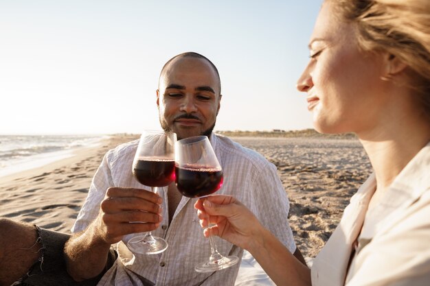 Portrait d'un jeune couple assis sur la plage et buvant du vin