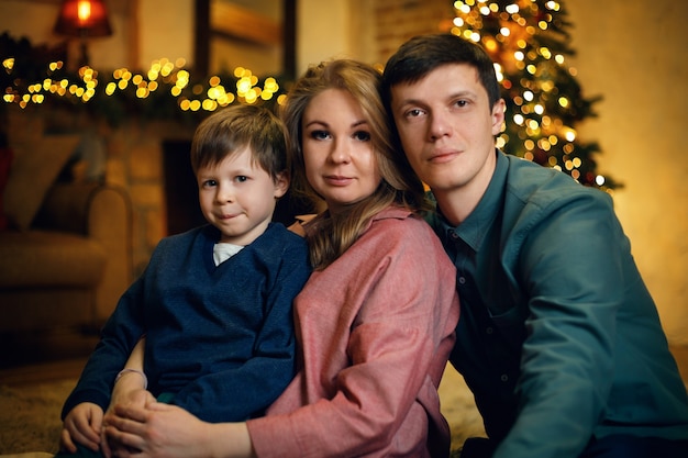 Portrait de jeune couple caucasien avec leur enfant posant sur le sol dans un intérieur de Noël confortable