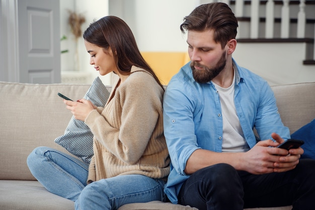 Portrait de jeune couple debout dos à l'autre et en regardant le téléphone.