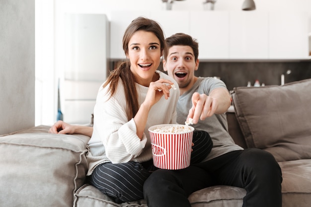 Portrait d'un jeune couple excité se détendre sur un canapé