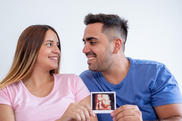 portrait d'un jeune couple hétérosexuel enceinte heureux montrant une impression échographique
