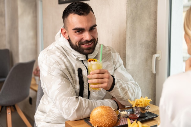 portrait, de, jeune couple, manger, hamburger, dans, restaurant, et, boire, cocktail, fruit passion, mojito