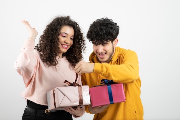 Photo portrait de jeune couple ouvrant des coffrets cadeaux sur un mur blanc.