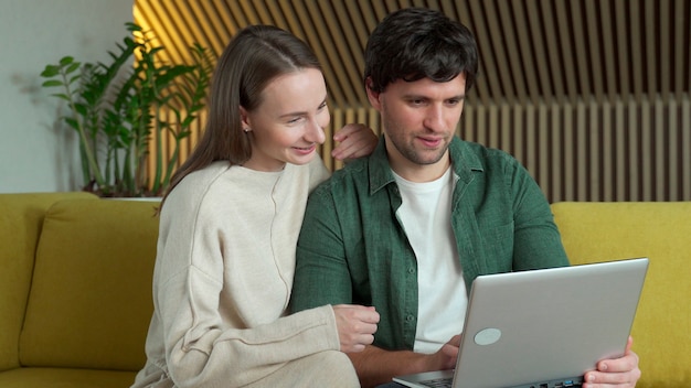 Portrait d'un jeune couple souriant à l'aide d'un ordinateur portable assis sur un canapé jaune à la maison