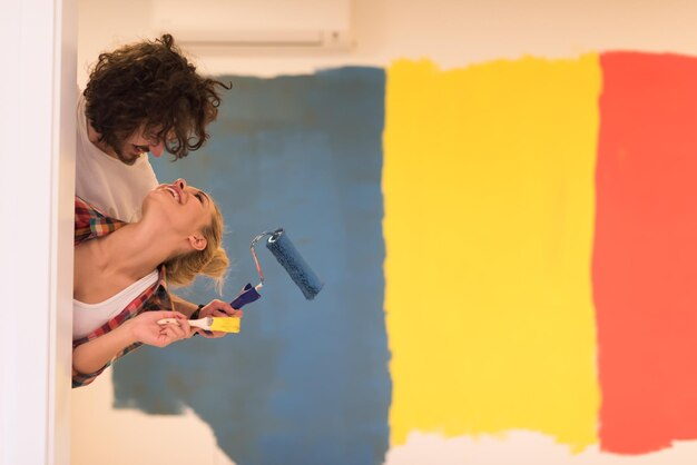 portrait d'un jeune couple souriant heureux peignant le mur intérieur de la nouvelle maison jetant un coup d'œil derrière le mur