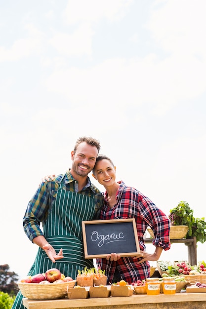 Portrait de jeune couple avec tableau vendant des légumes biologiques