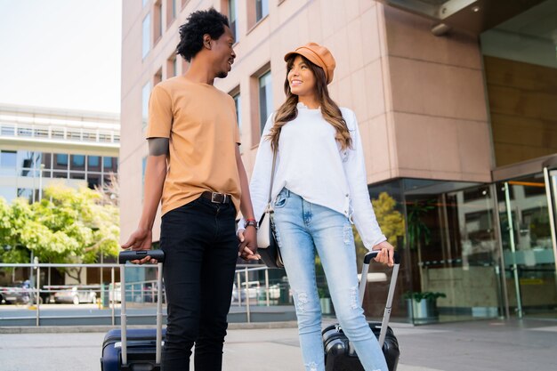 Portrait de jeune couple de touristes transportant une valise tout en marchant à l'extérieur dans la rue.