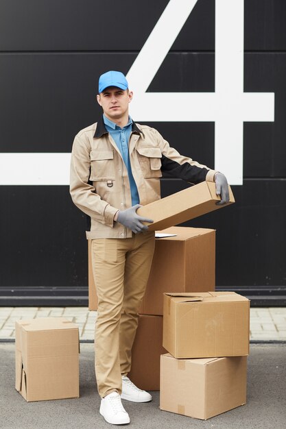 Portrait de jeune courrier en uniforme regardant la caméra tout en travaillant avec des colis en entrepôt