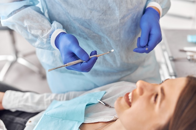 Portrait de jeune dentiste en gants examinant les dents d'une cliente à l'hôpital.