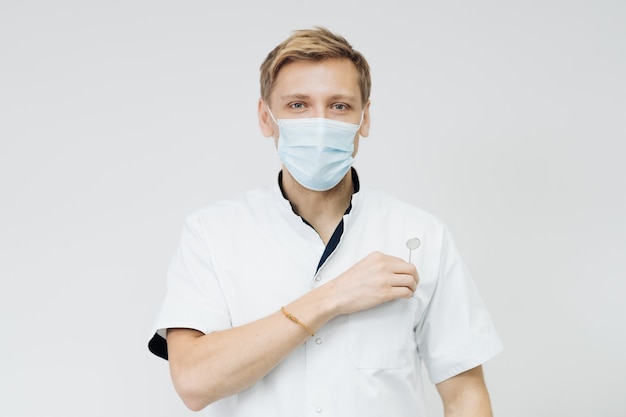 Portrait d'un jeune dentiste masculin porter un masque stérile isolé sur mur blanc