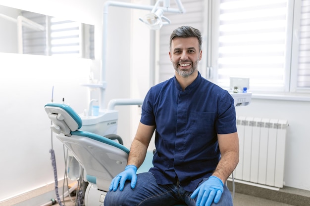 Portrait d'un jeune dentiste souriant assis dans sa clinique