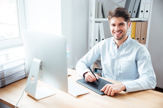 Portrait d'un jeune designer souriant travaillant et utilisant une tablette graphique au bureau