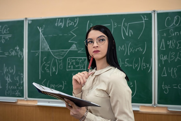 Portrait de jeune enseignante contre tableau noir avec formule mathématique en classe
