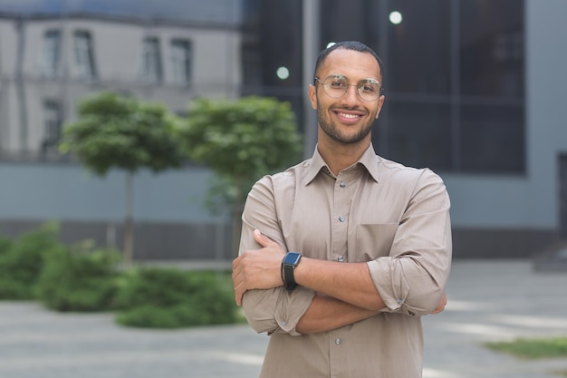 Portrait d'un jeune étudiant hispanique souriant et regardant la caméra près du campus universitaire avec