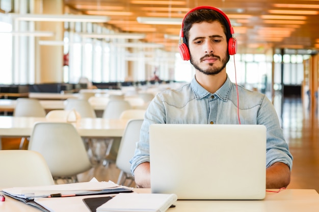 Portrait de jeune étudiant masculin utilisant un ordinateur portable et apprenant en ligne à la bibliothèque universitaire. Concept d'éducation et de style de vie.