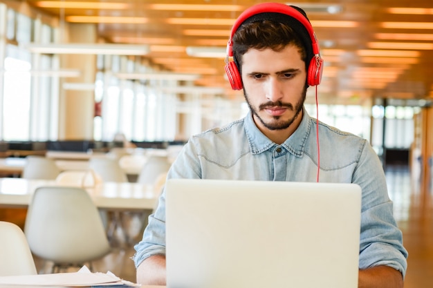 Portrait de jeune étudiant masculin utilisant un ordinateur portable et apprenant en ligne à la bibliothèque universitaire. Concept d'éducation et de style de vie.