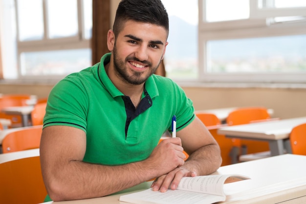Portrait de jeune étudiant universitaire masculin arabe avec livre assis dans la salle de classe seul