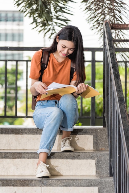 Portrait d'une jeune étudiante asiatique heureuse assise pendant qu'elle lit un livre à l'université, retour à l'éducation au concept universitaire