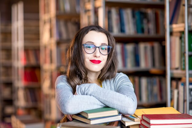 Portrait de jeune étudiante enthousiaste étudiant avec beaucoup de livres à la bibliothèque