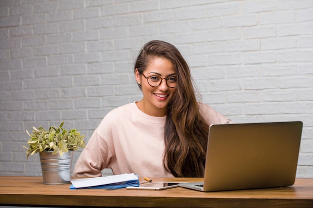 Portrait de jeune étudiante latine femme assise sur son bureau avec les mains sur les hanches, debout