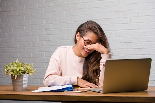 Portrait de jeune étudiante latine femme assise sur son bureau en riant et s&#39;amusant