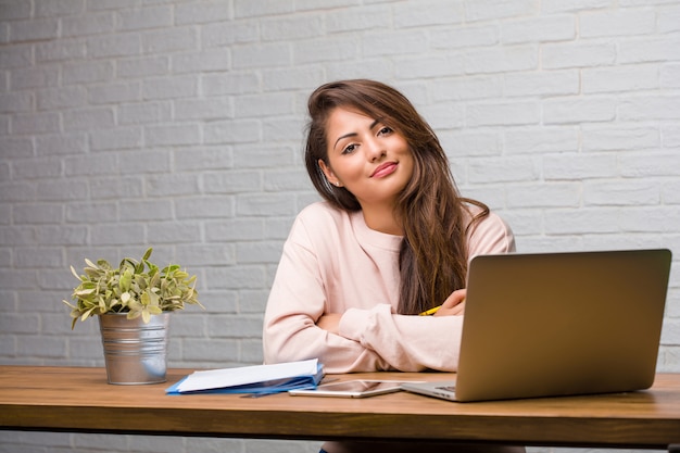 Portrait de jeune étudiante latine femme assise sur son bureau en traversant ses bras