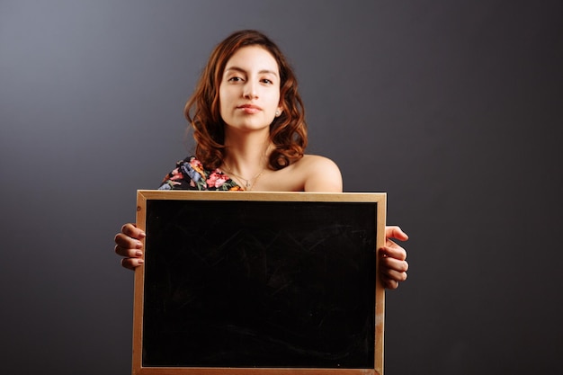 Portrait de jeune étudiante latino-américaine tenant un tableau vide isolé sur gris