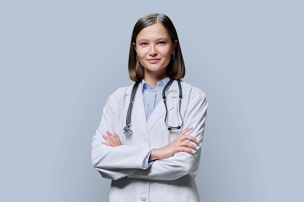 Portrait d'une jeune étudiante en médecine en manteau blanc sur fond gris