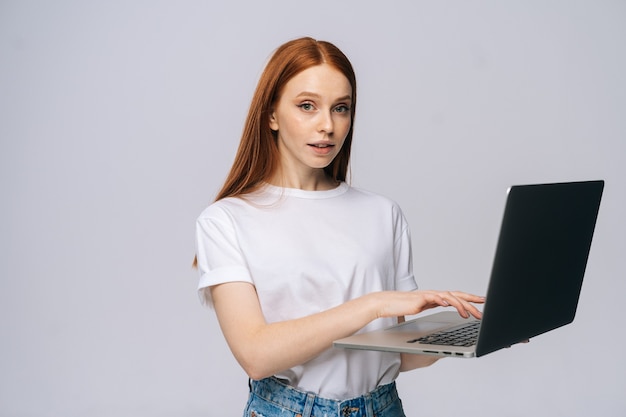 Portrait d'une jeune étudiante réussie tenant un ordinateur portable et tapant sur fond isolé