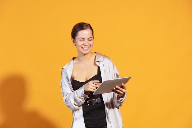 Portrait d'une jeune étudiante souriante dans des vêtements décontractés posant avec une tablette isolée sur jaune